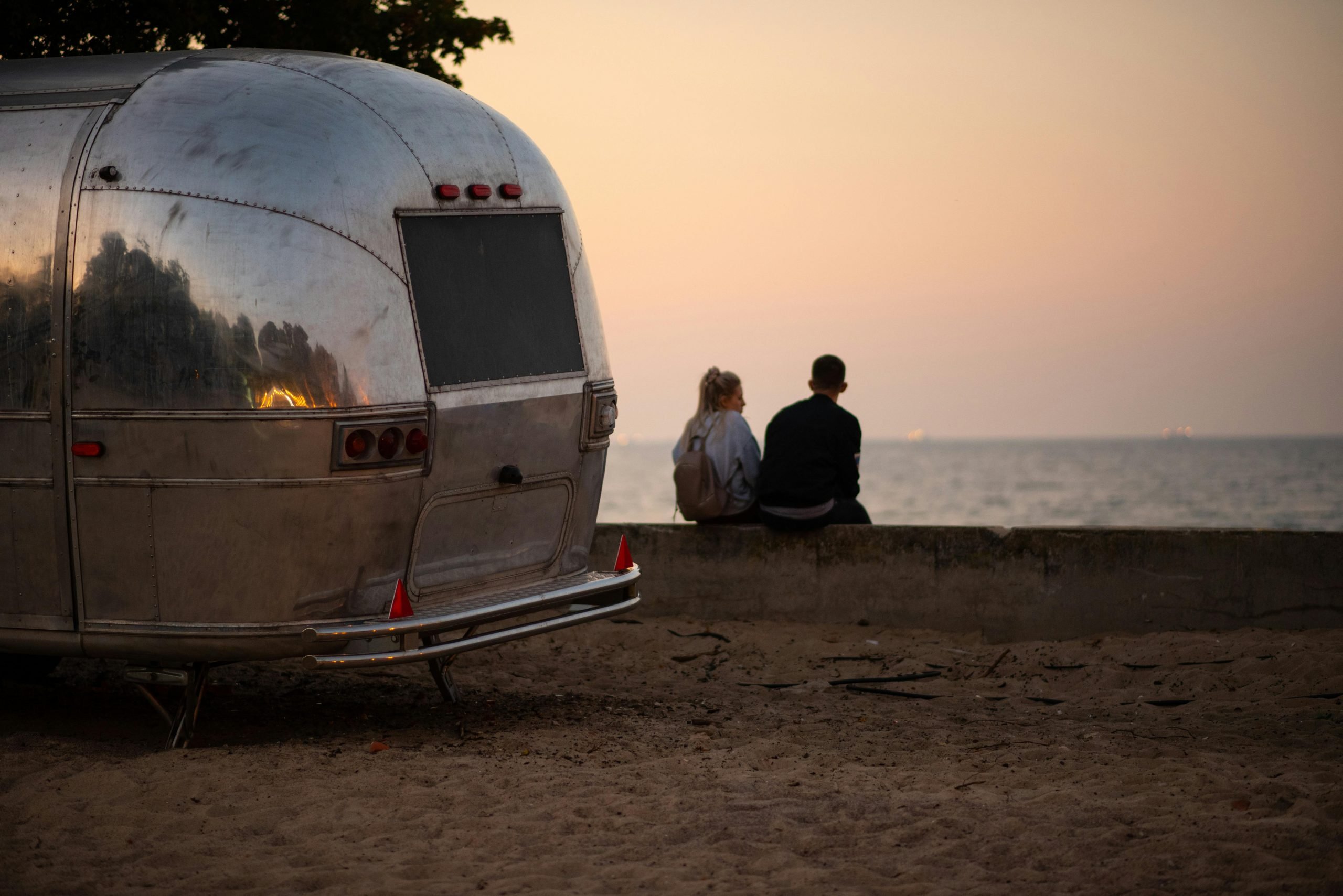 A couple watching the sunset while sitting in front of a trailer.