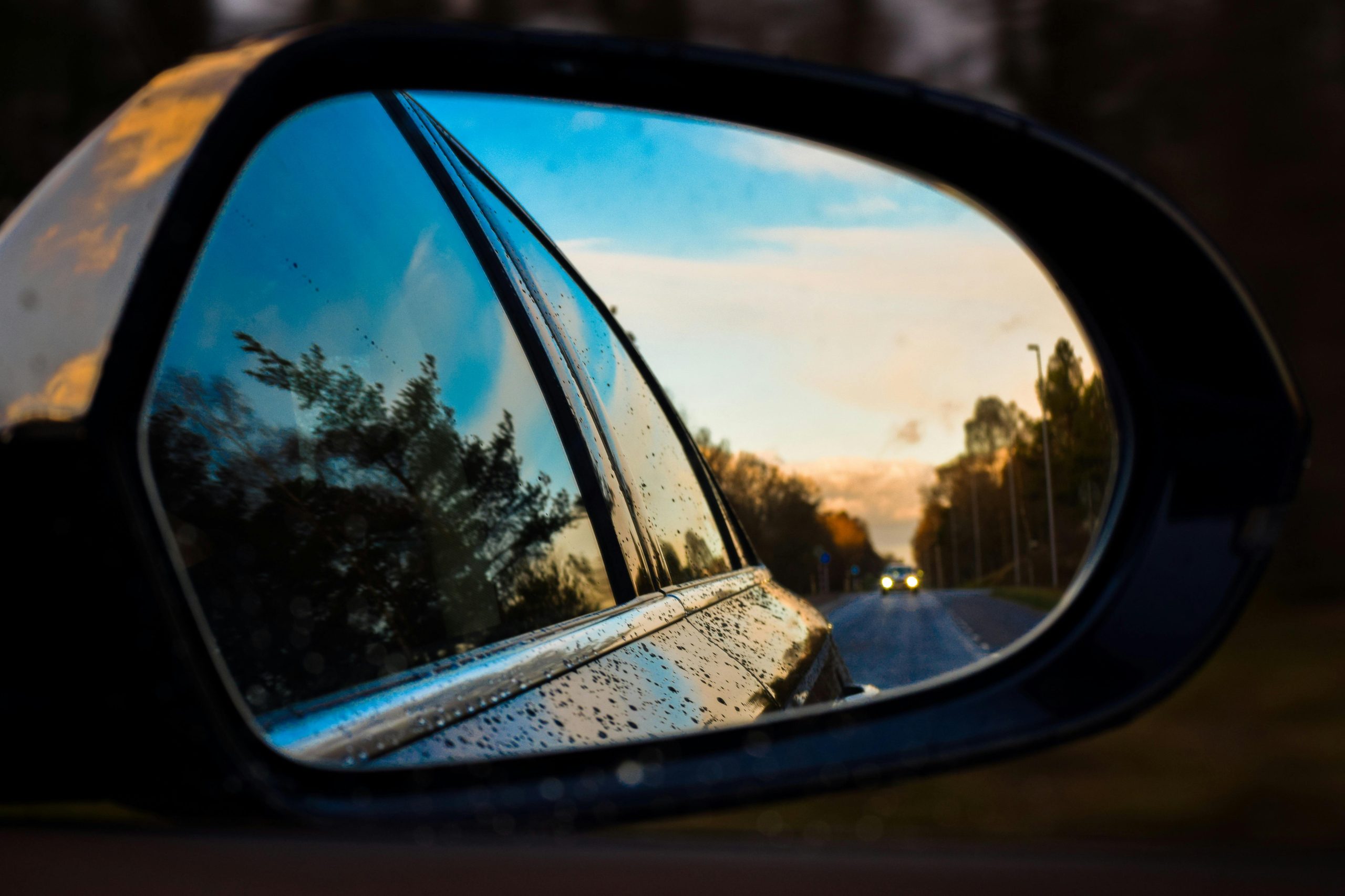 View of a vehicle's side mirror as it drives down a road in spring