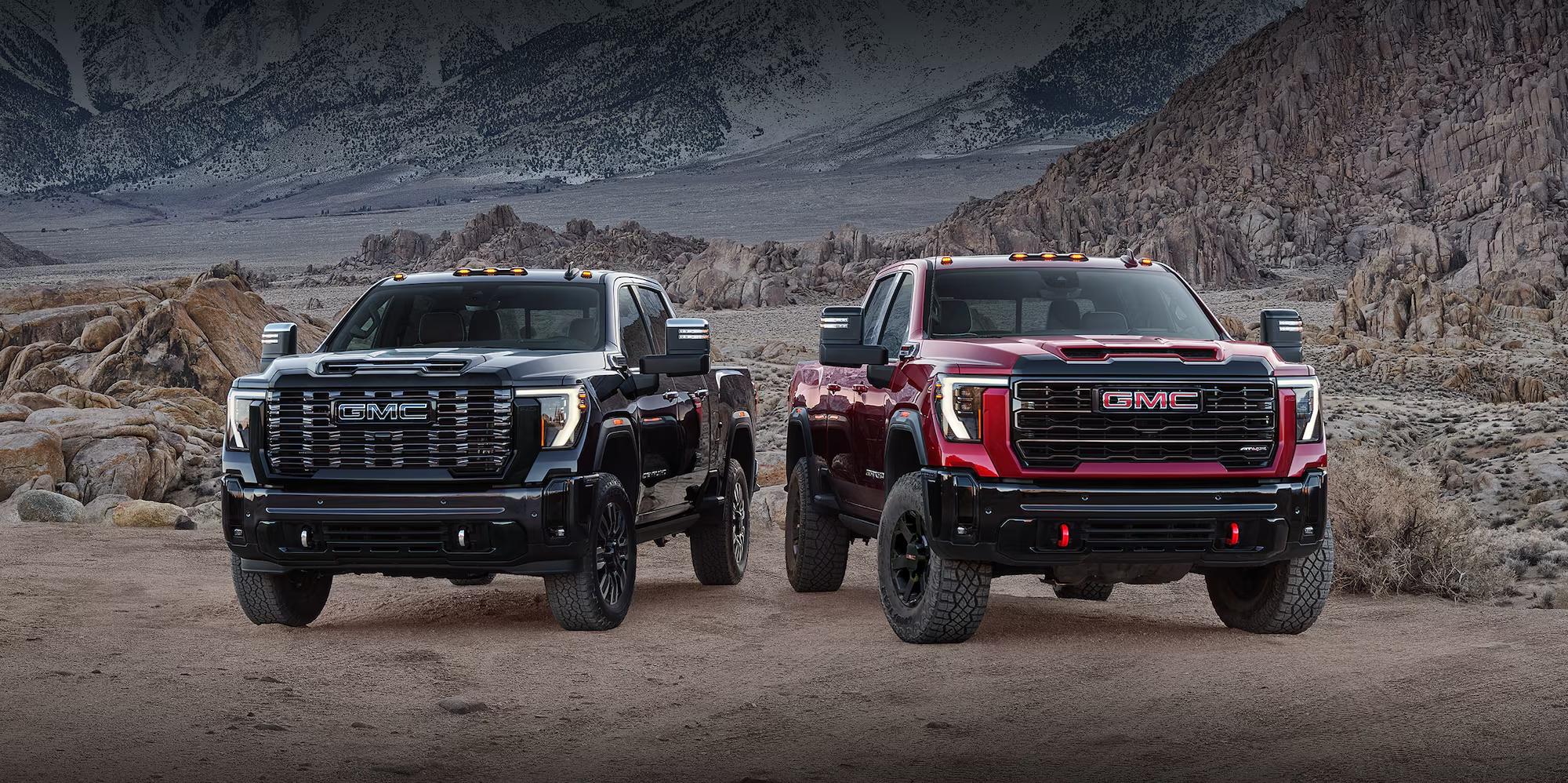 Two 2027 GMC Sierra HD trucks in a rugged mountain landscape