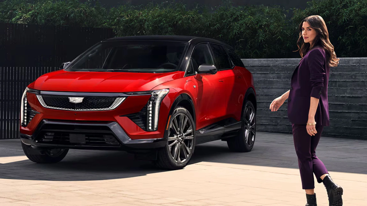 Cadillac Optiq 2026 rouge accompagné d’une conductrice.